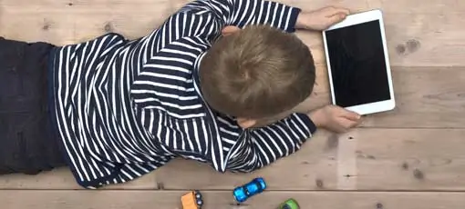 Kind liegt zwischen Spielzeug und schaut auf Tablet
